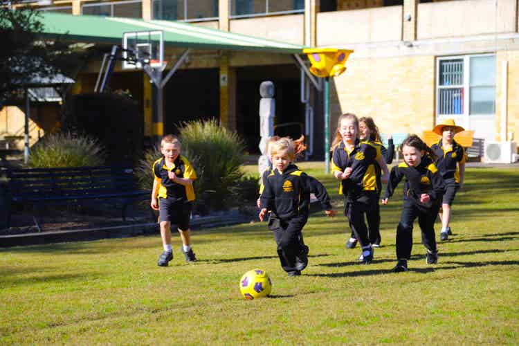 a group of students chasing a soccer ball on the school oval