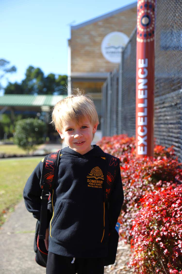 a male student with their bag on standing out the front of the school