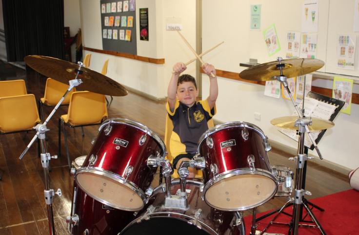 a male student holding drum sticks while sitting at a set of drums